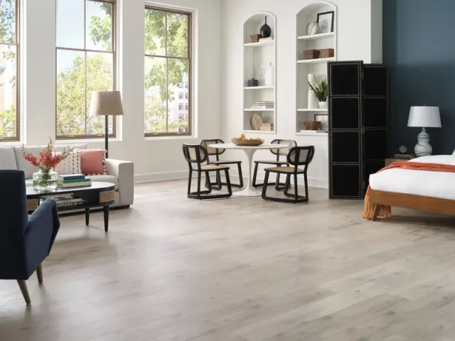 Open loft with living, dining, and bedroom areas over light wood-look flooring.
