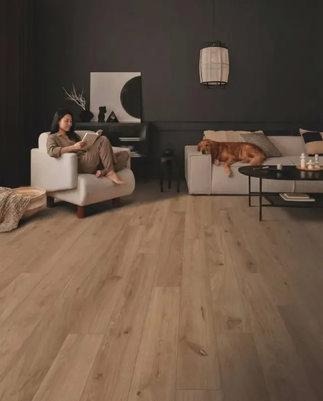 Woman reading with her dog in a dark living room over wood-look flooring.
