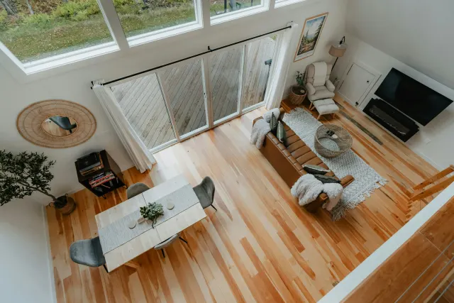 Aerial view of an open loft living and dining space with a leather sofa, dining table, and warm honey-toned hardwood flooring.