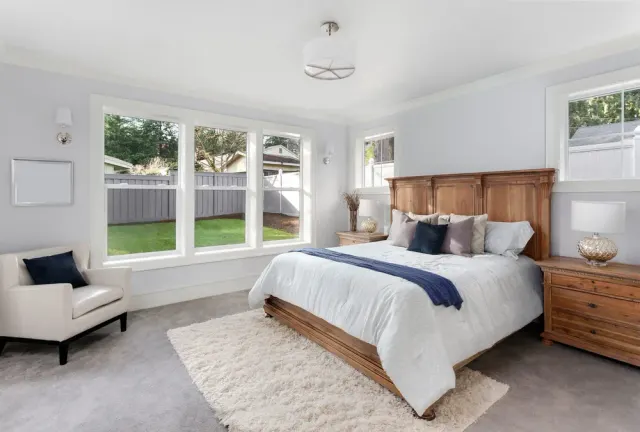 Bedroom with a wood bed frame and a cream shag area rug layered over carpet flooring.